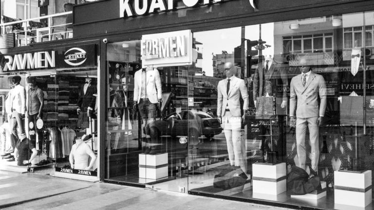 Black and white image of a men's fashion storefront showcasing elegant suits with mannequins prominently featured.